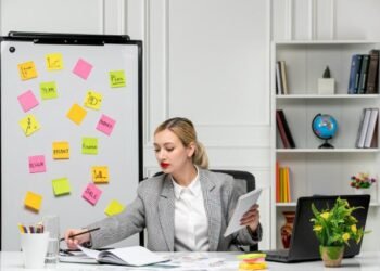 Marketing young cute blonde girl in grey suit in the office writing something in notepad.