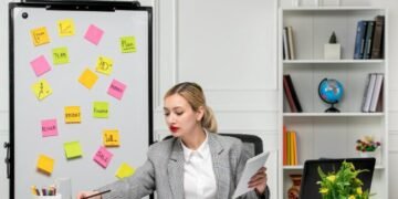 Marketing young cute blonde girl in grey suit in the office writing something in notepad.