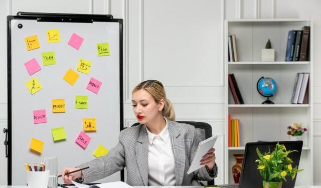 Marketing young cute blonde girl in grey suit in the office writing something in notepad.