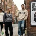 Streetwear-inspired photo of three people walking down a brick-paved alleyway past a poster titled "How Justin Bieber Skylark Connects Celebrity Image With Streetwear".