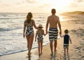 Family of four in coordinated navy and cream swimwear walking along a beach