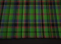 Close-up of dark green and navy tartan fabric, crossed by fine red and yellow lines in a repeating plaid pattern with subtle folds and a traditional feel.