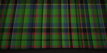 Close-up of dark green and navy tartan fabric, crossed by fine red and yellow lines in a repeating plaid pattern with subtle folds and a traditional feel.
