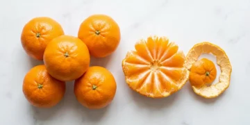 Small mandarin oranges on a white surface with one peeled into segments