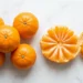 Small mandarin oranges on a white surface with one peeled into segments