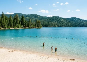 Clear lake with a sandy public swim beach and buoyed swimming area on a summer day