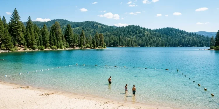 Clear lake with a sandy public swim beach and buoyed swimming area on a summer day